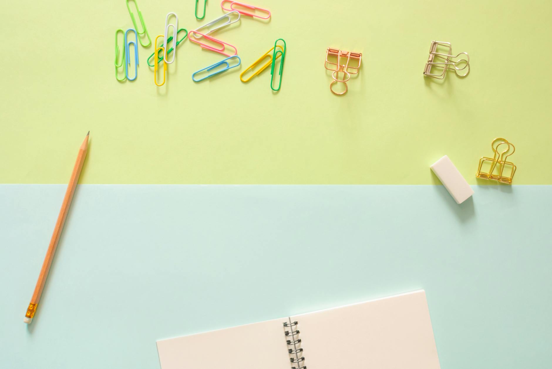 assorted color metal clips on table beside pencil and notebook